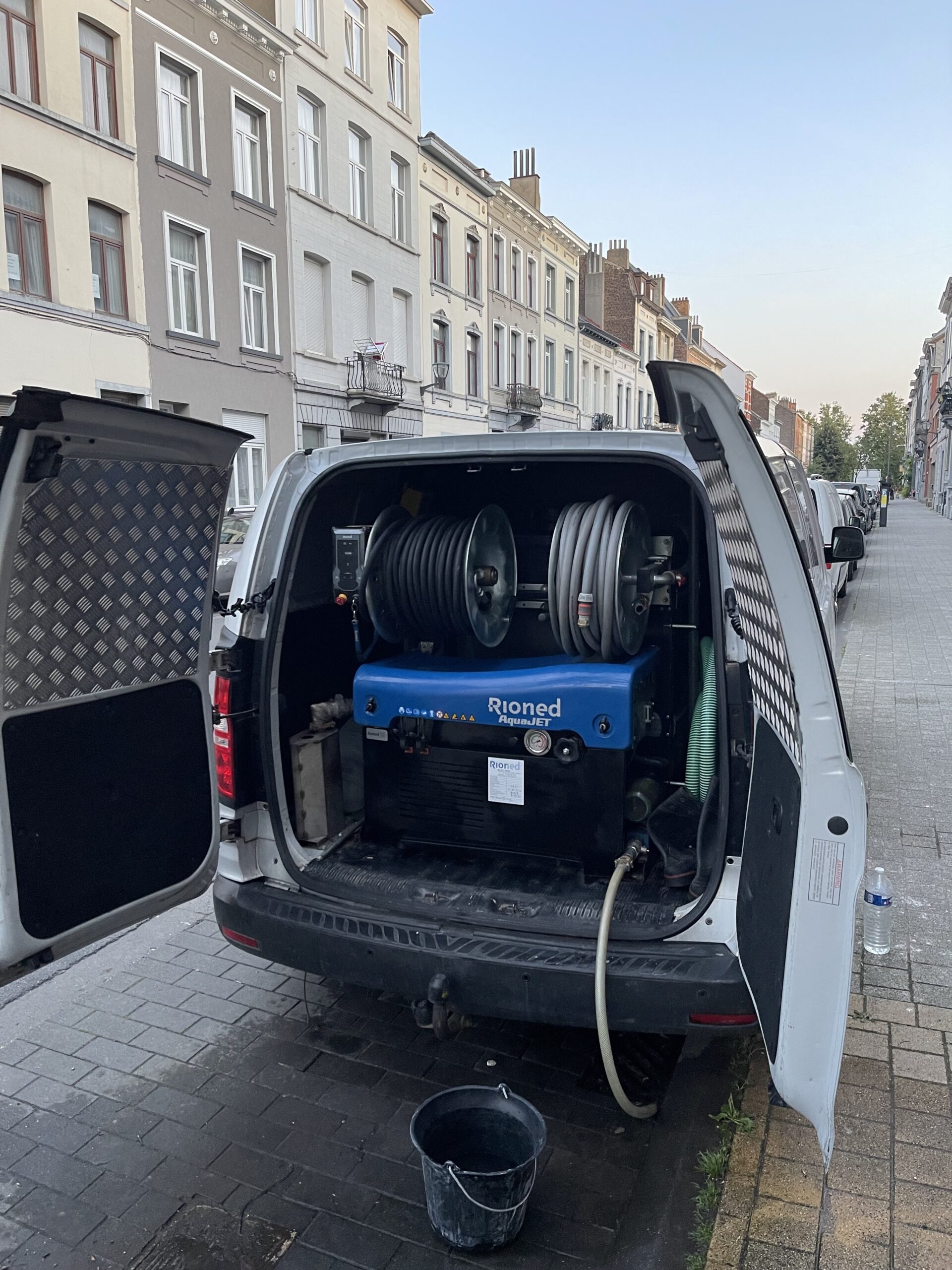 Bestelwagen van STB met de Rioned-hogedrukreiniger, deuren open in een Brusselse straat